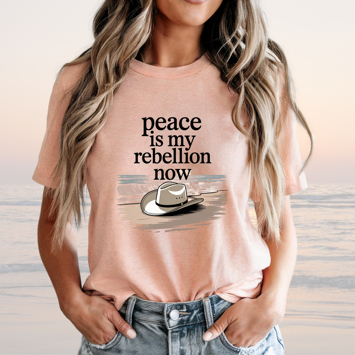 Woman wearing peach loose-fit Peace is My Rebellion Now Tee with cowboy hat graphic and text, styled with jeans.
