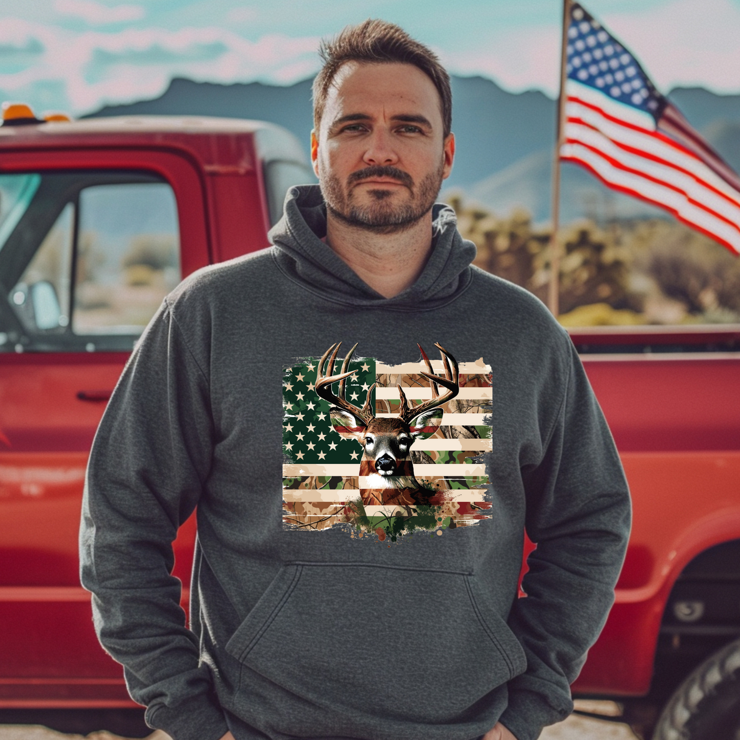 Man wearing a hoodie with a deer and American flag design, standing in front of a red truck and American flag.
