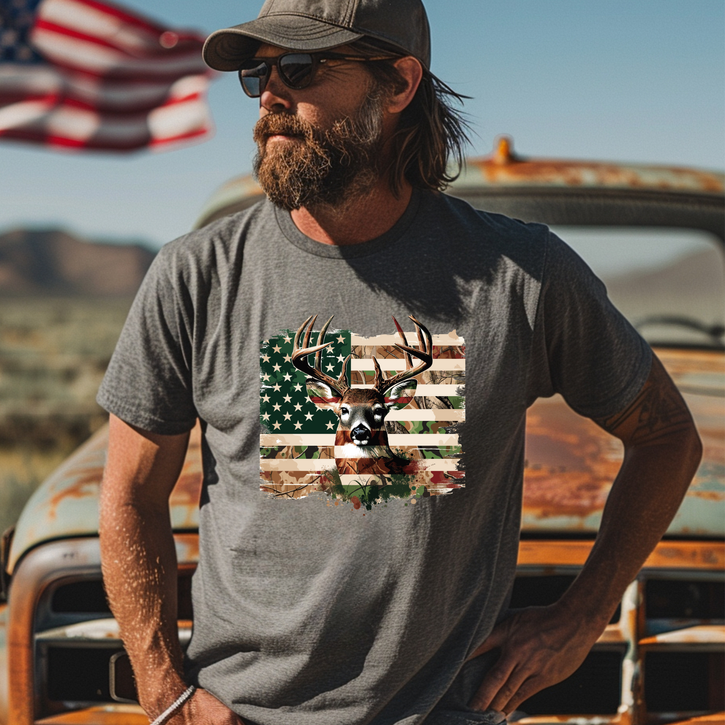 Man wearing a t-shirt with a deer and American flag design, standing in front of an old truck and American flag.