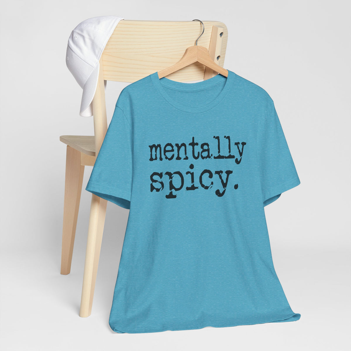 Blue t-shirt with 'mentally spicy' text on a wooden chair against a white background