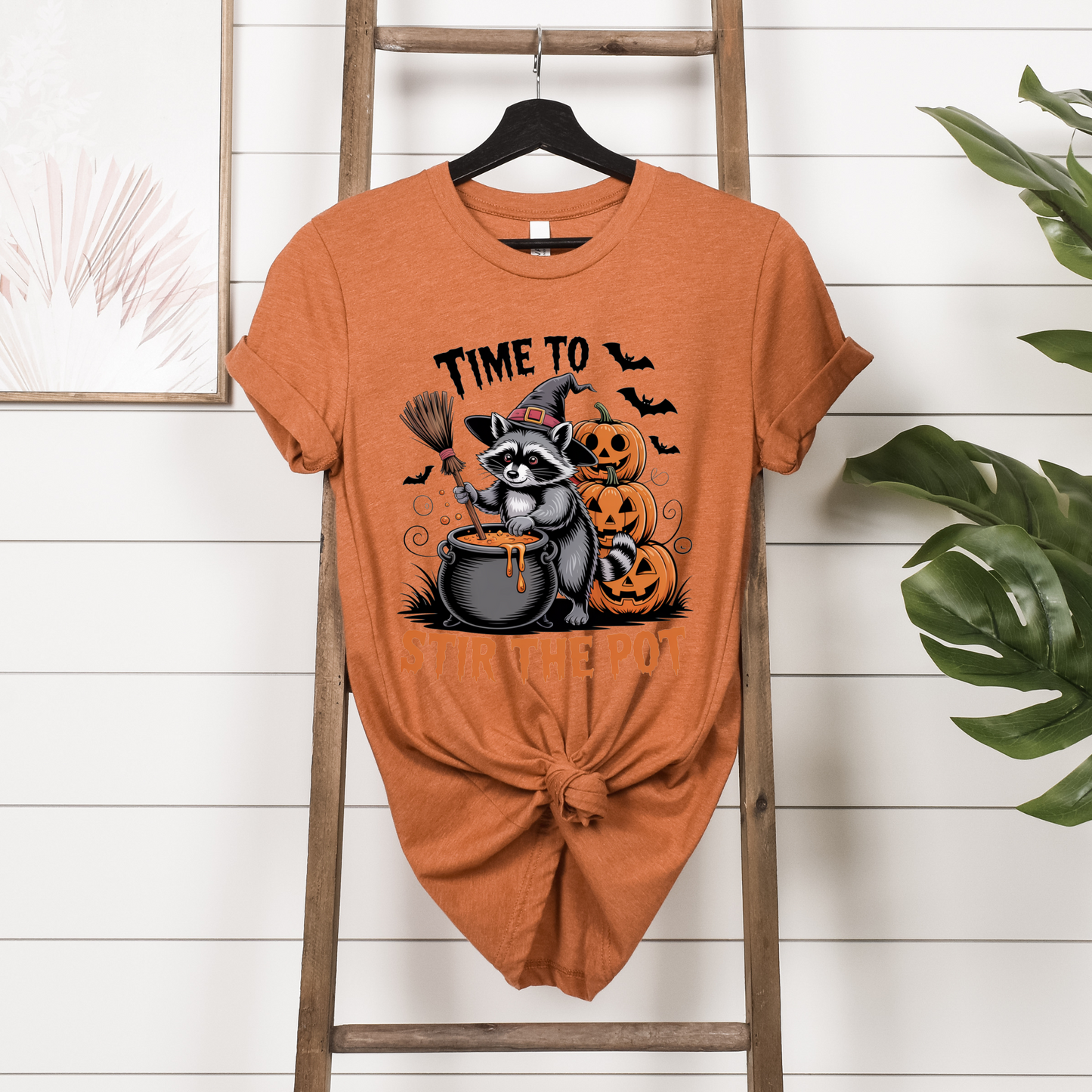 Orange t-shirt with Halloween-themed design featuring a raccoon and pumpkins on a wooden ladder.
