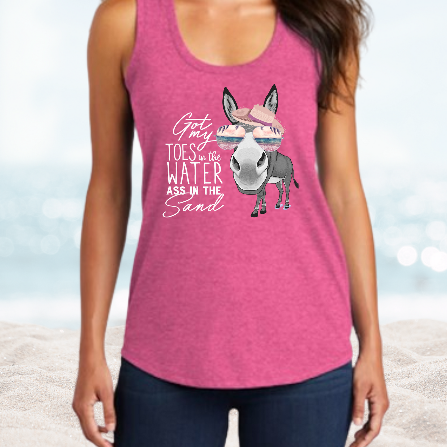Woman wearing a pink Vacation Toes in the Water Ass in the Sand tank top with a donkey graphic and beach-themed text at the beach