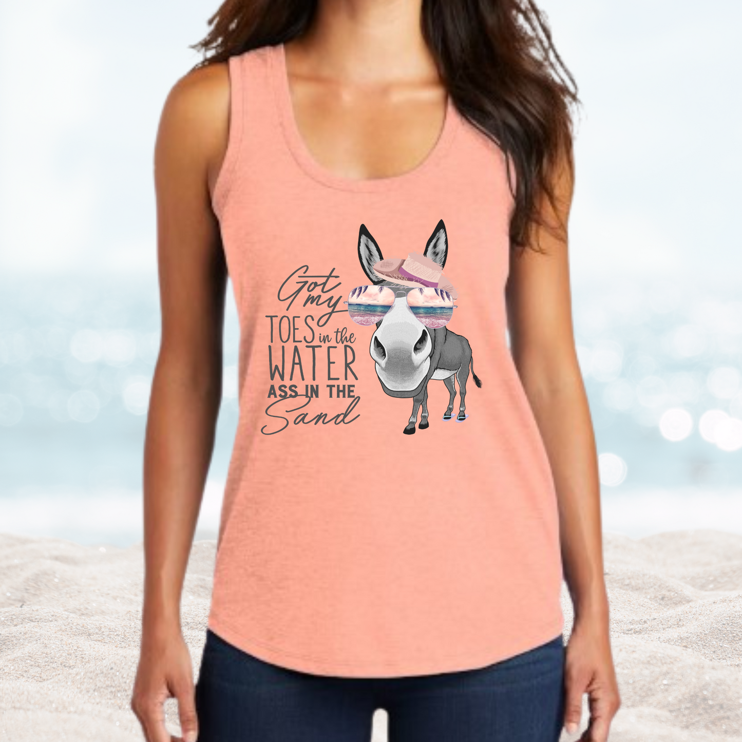 Woman wearing peach tank top with "Got my toes in the water ass in the sand" text and donkey graphic, beach background