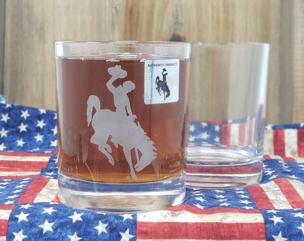 Wyoming University Whiskey Glass Set with etched Cowboy logo on American flag backdrop.