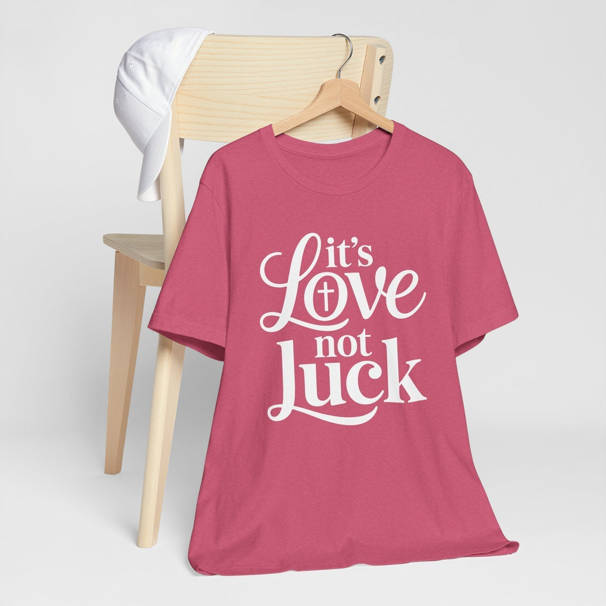 Graphic tee in rose pink cotton with white script and bold lettering reading “It’s Love Not Luck,” love in faith shirt