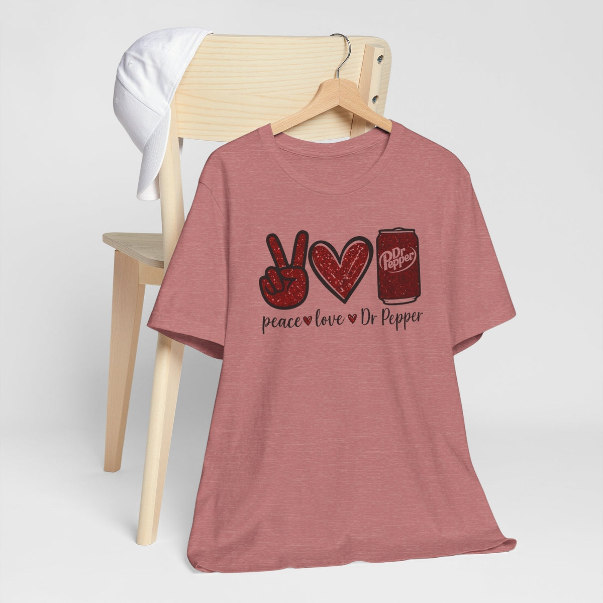 Graphic T-shirt for a soda lover in muted heather pink, with a peace sign, heart, Dr Pepper can and lettering