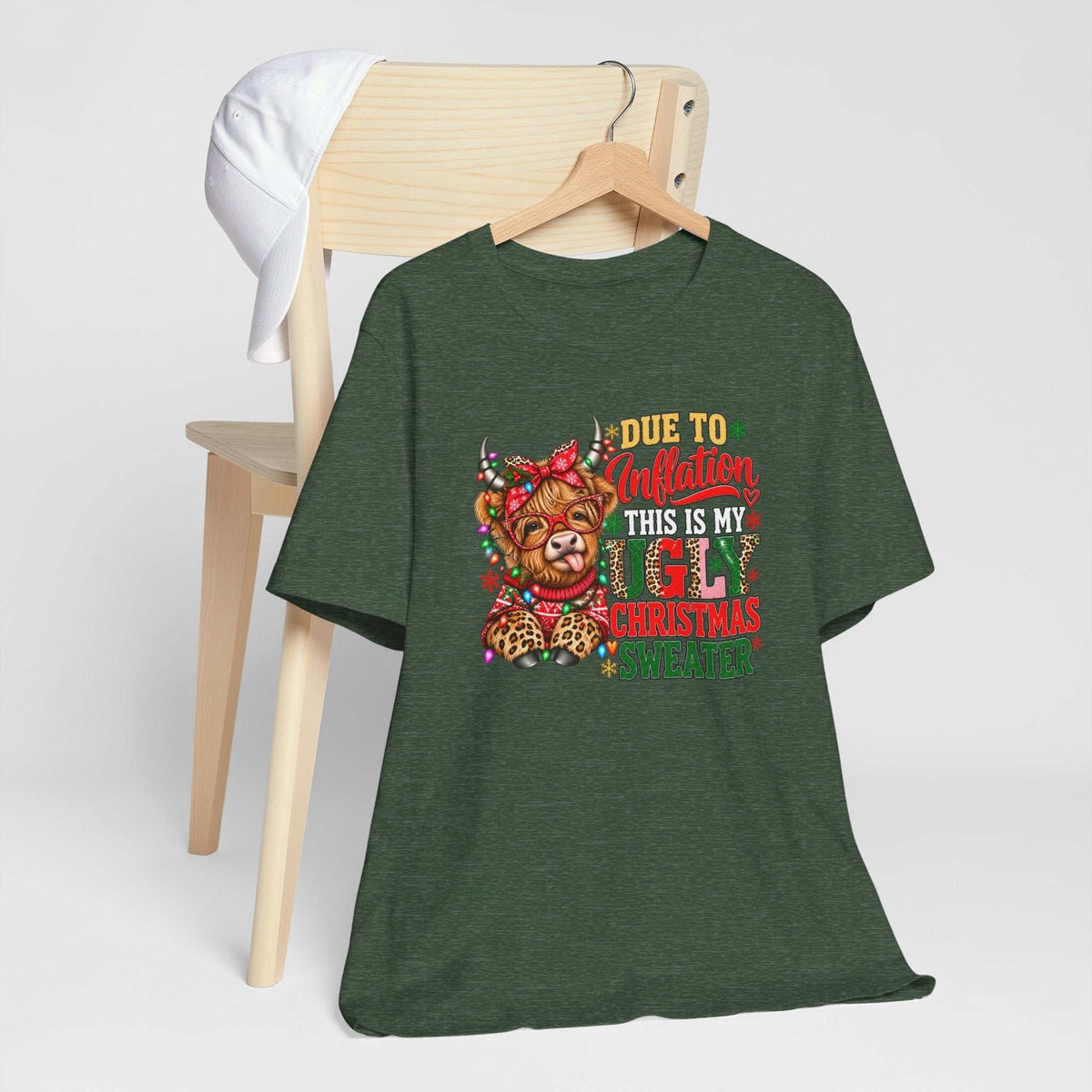 ugly christmas shirt in dark heather green with a colorful Highland cow, festive lights and “Due to Inflation” text