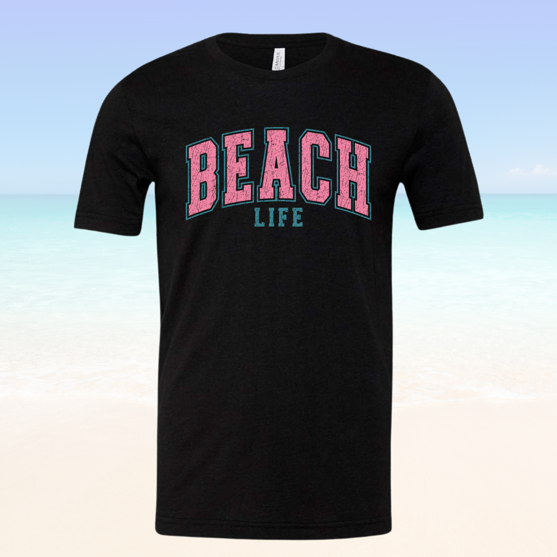 Beach Life Vibe Tee with pink and blue text on a black background, against a beach setting.