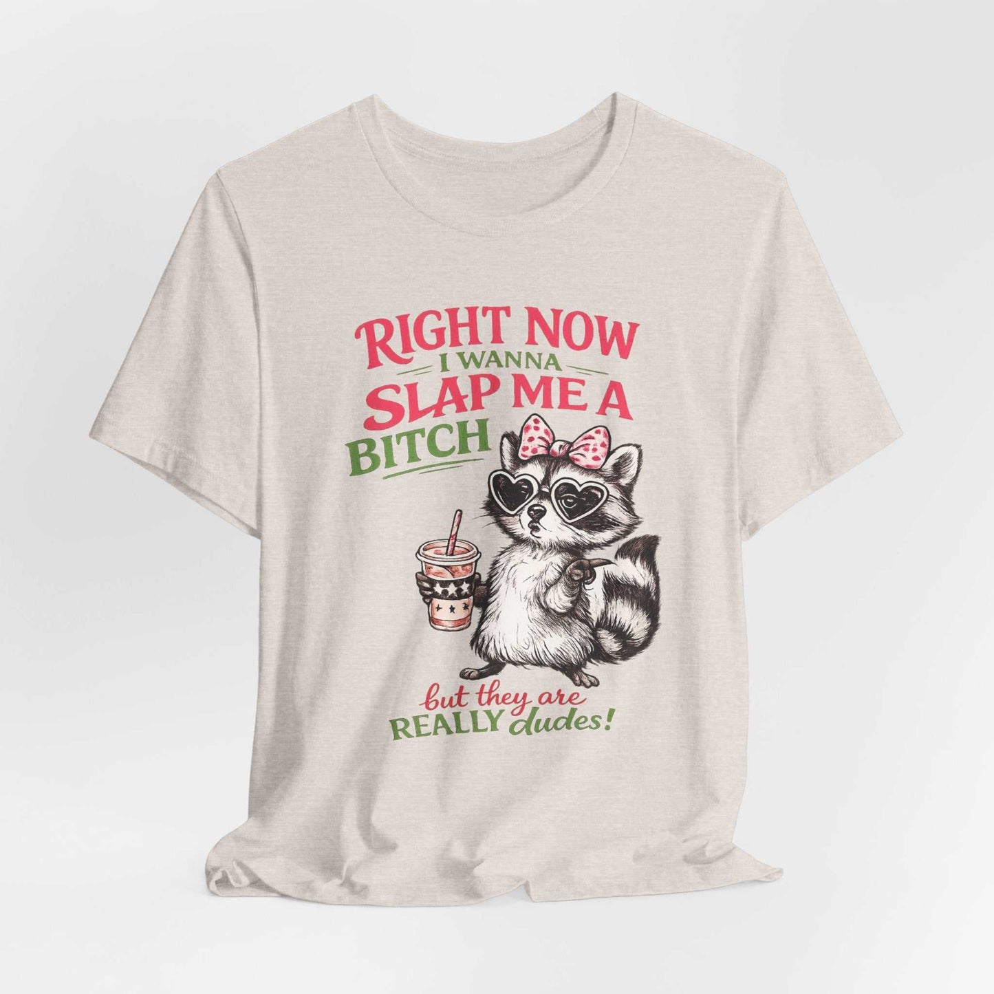 Graphic tee featuring sassy raccoon with sunglasses and pink bow saying "Right Now I Wanna Slap Me a BITCH… But They Are REALLY dudes!" in distressed pink and sage lettering