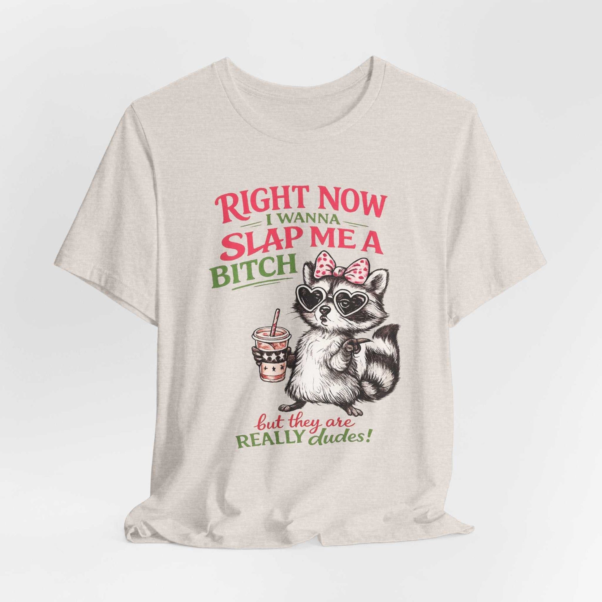 Graphic tee featuring sassy raccoon with sunglasses and pink bow saying "Right Now I Wanna Slap Me a BITCH… But They Are REALLY dudes!" in distressed pink and sage lettering