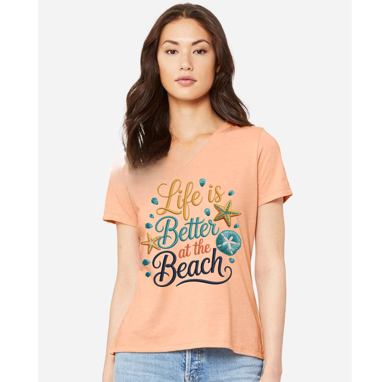 Women's V-neck tee with "Life Is Better at the Beach" faux embroidered cross-stitch design featuring seashells and starfish in coastal colors.