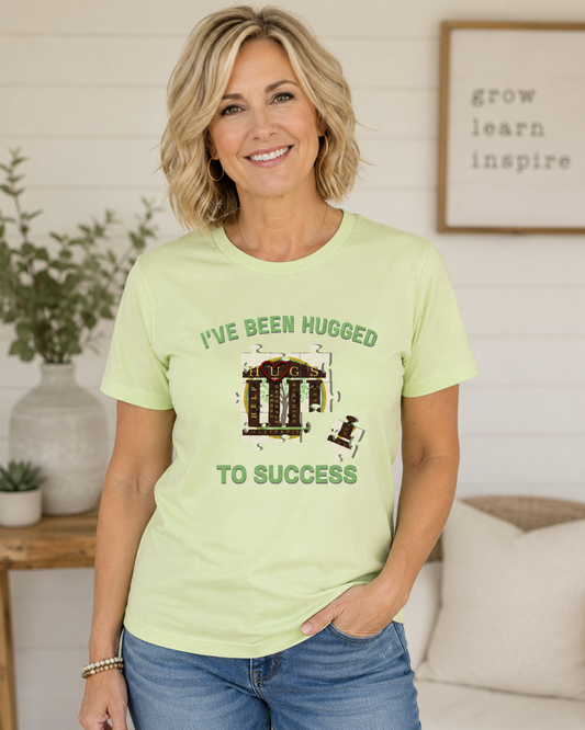 I've Been Hugged to Success tee with puzzle-piece design symbolizing growth and connection, soft Bella Canvas fabric, perfect for HUGS graduates and affiliates.
