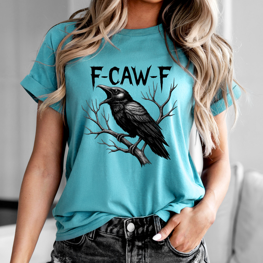 Person wearing a turquoise t-shirt with a black crow graphic and 'F-CAW-F' text.