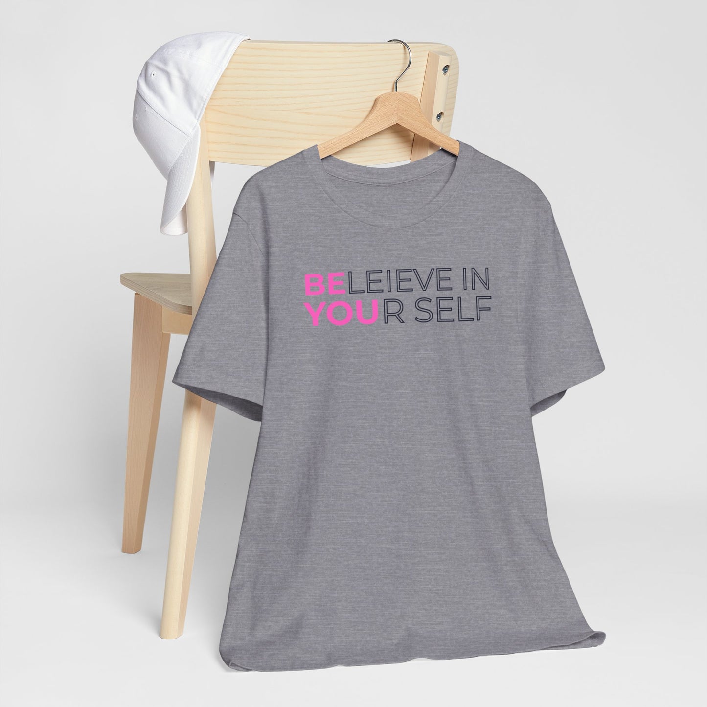 Gray t-shirt with 'BELIEVE IN YOURSELF' text on a wooden chair against a white background