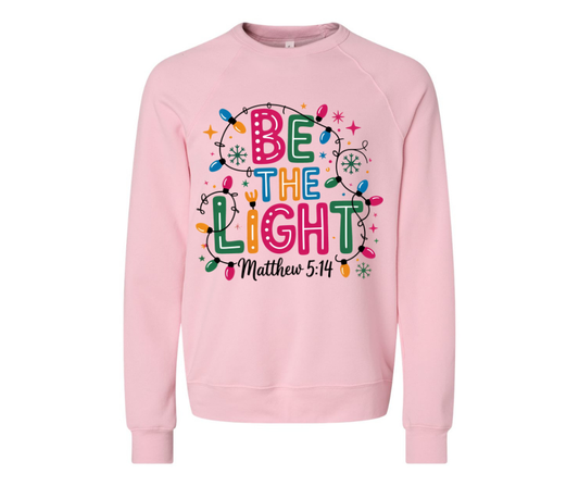 Soft heather pink “Be The Light” sweatshirt. Cozy unisex fit, inspirational Matthew 5:14 design. Perfect for Christmas, gifts, and winter comfort.