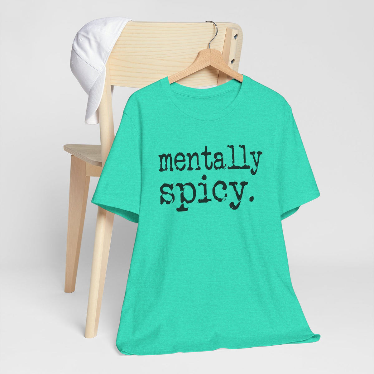 Green t-shirt with 'mentally spicy' text on a wooden chair against a white background