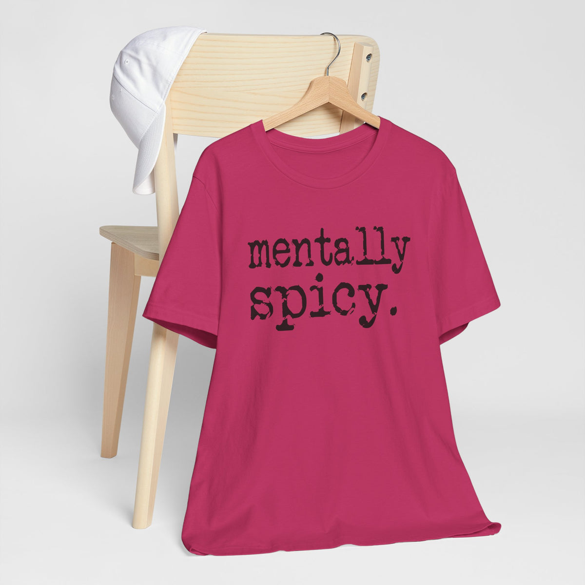 Pink t-shirt with 'mentally spicy' text on a wooden chair against a white background