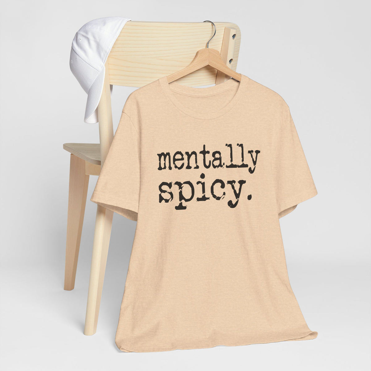 Beige t-shirt with 'mentally spicy' text on a hanger against a white background