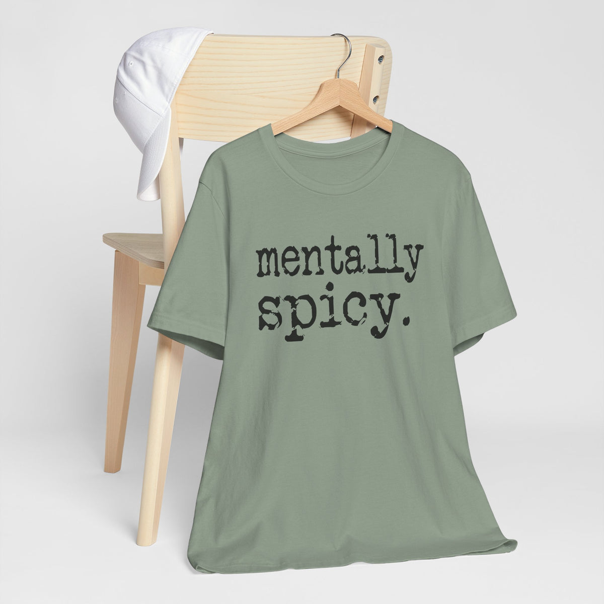Green t-shirt with 'mentally spicy' text on a wooden chair against a white background