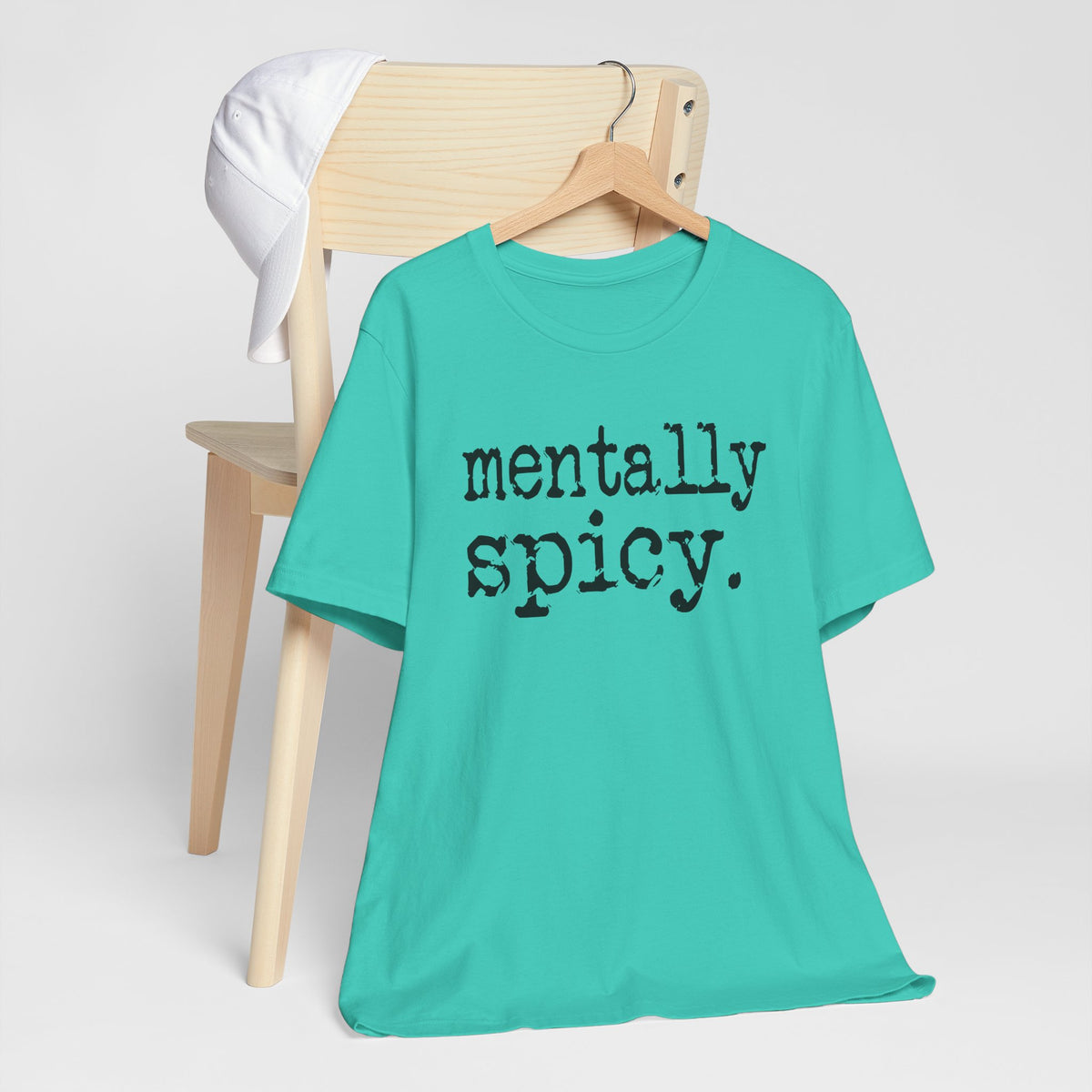 Turquoise t-shirt with 'mentally spicy' text on a wooden chair against a white background