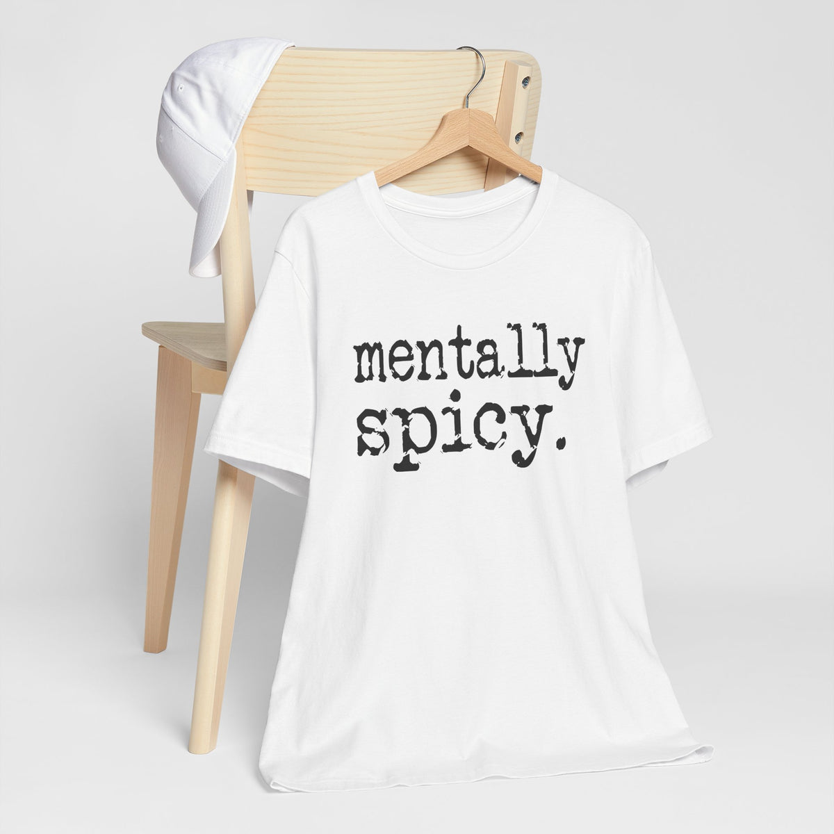 White t-shirt with 'mentally spicy' text on a wooden chair against a white background