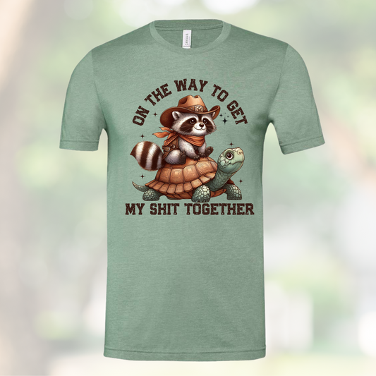 Unisex shirt with "On my Way to Get My Shit Together" text, featuring a raccoon riding a turtle.