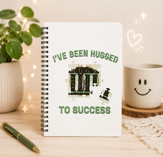 I've Been Hugged to Success spiral notebook with puzzle-piece design, durable plastic cover, and metal spiral binding for journaling and note-taking