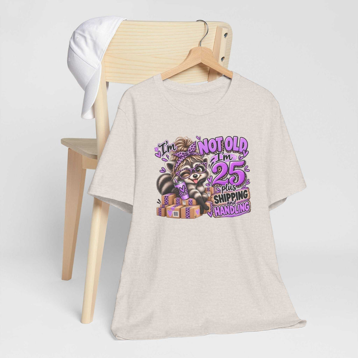 Adult humor tshirt in light heather beige featuring a colorful raccoon graphic, purple leopard-print accents, and birthday slogan