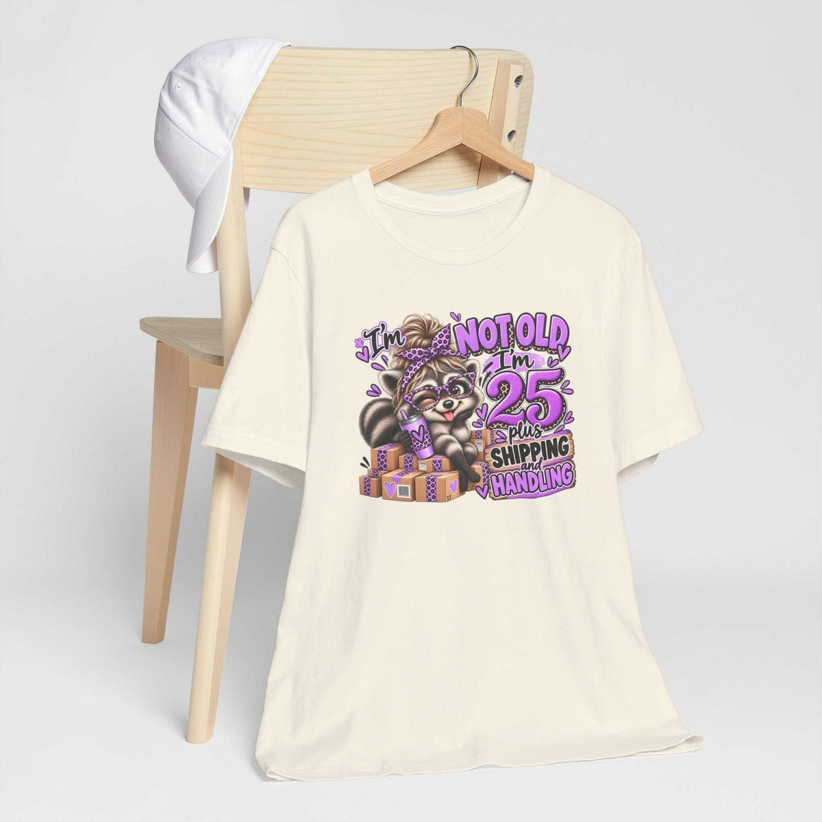 adult humor tshirt in cream with a colorful raccoon graphic, purple leopard-print accents, and birthday shipping joke