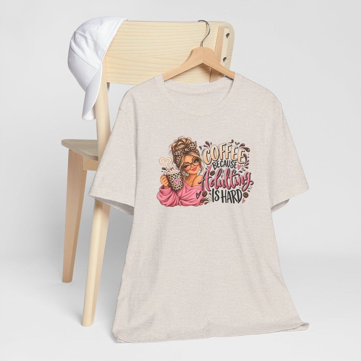 Adulting tshirt in light beige with a colorful coffee-loving woman graphic and playful “Coffee Because Adulting Is Hard” lettering