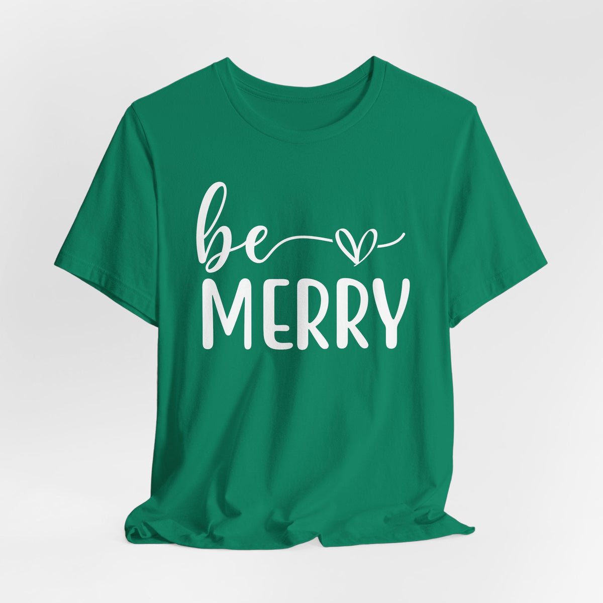 Be Merry Christmas Graphic Tee in green cotton-blend fabric, featuring white script and block lettering with a heart accent