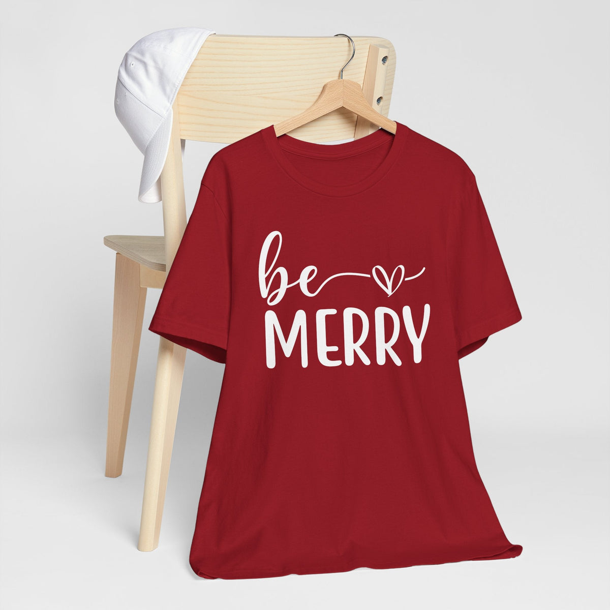 Be Merry Christmas Graphic Tee in red cotton, featuring white script and block lettering with a heart detail