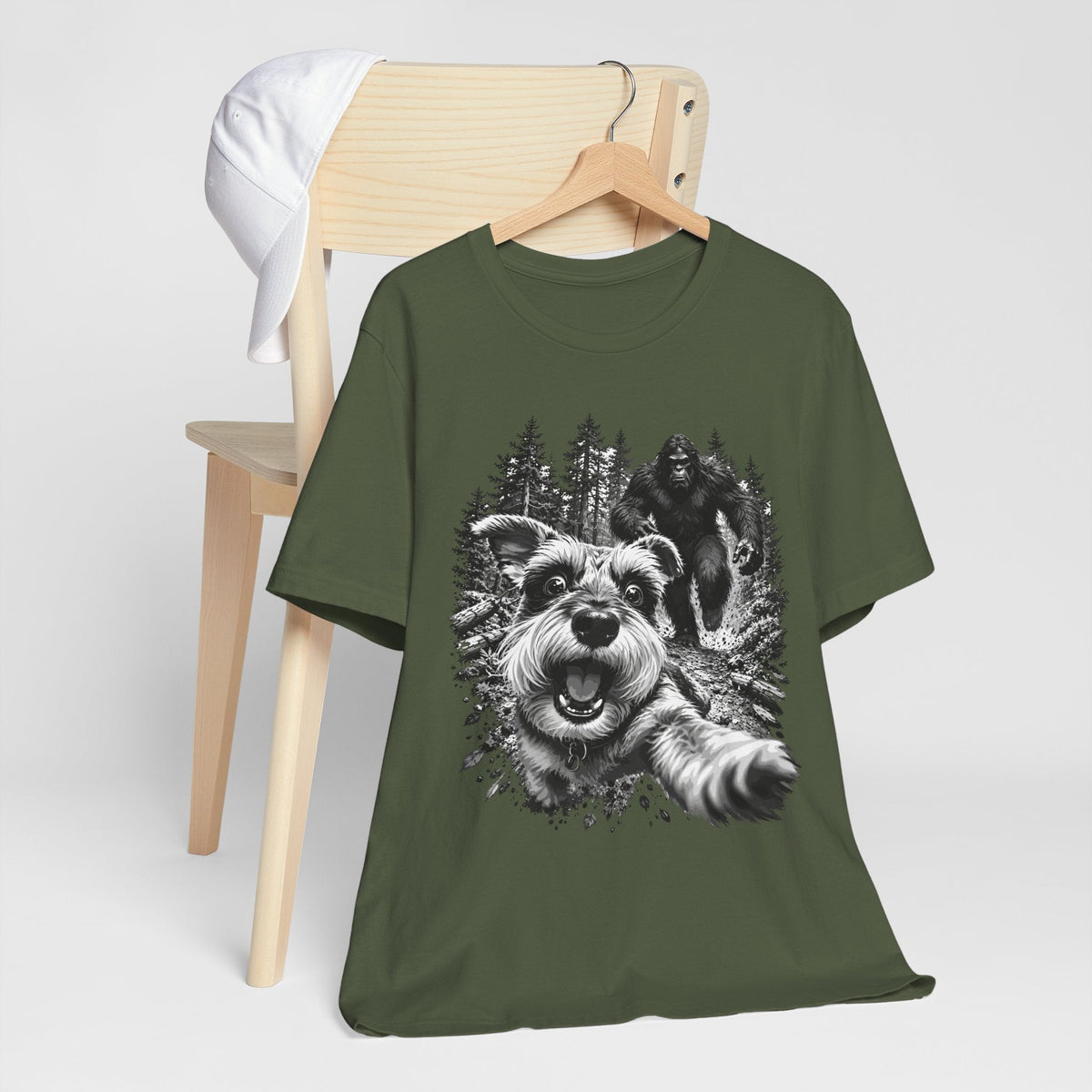 bigfoot shirt in dark olive green with a black and white graphic of a playful dog and Bigfoot in a forest