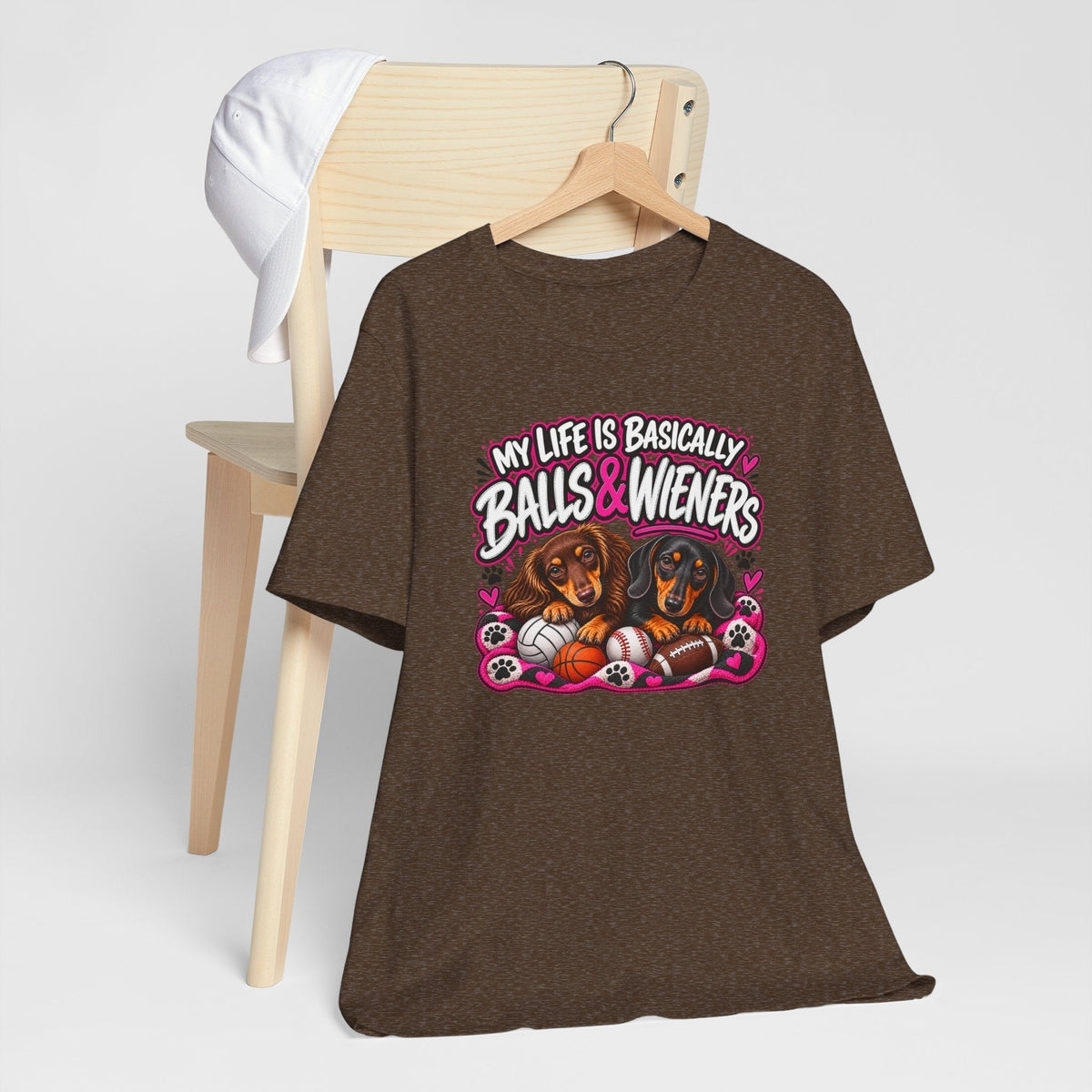 funny dachshund graphic tee in dark brown fabric with pink, white and black lettering, two dogs and sports balls
