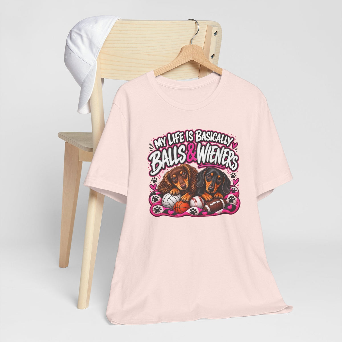 funny dachshund graphic tee in pale pink, featuring two dachshunds, colorful sports balls and bold lettering