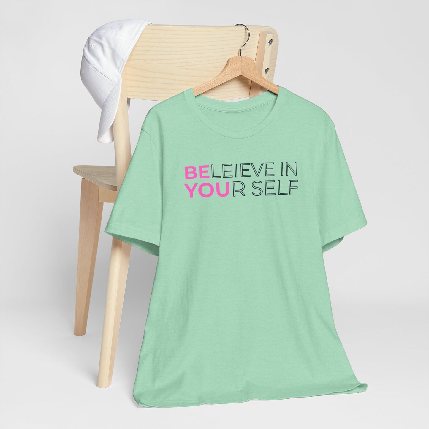 Mint green t-shirt with 'BELIEVE IN YOURSELF' text on a wooden chair against a white background
