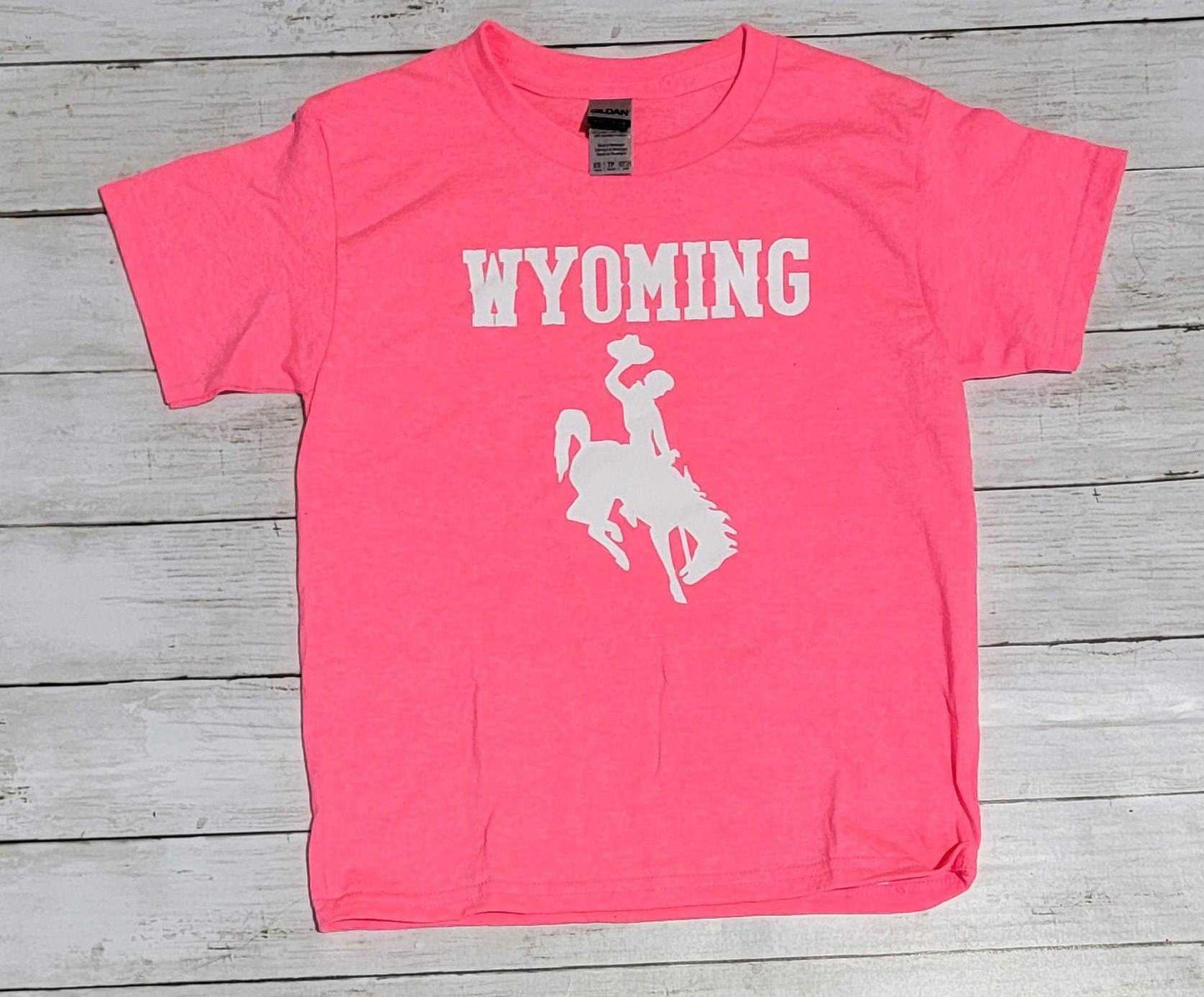Hot pink Wyoming Cowboys youth T-shirt with white logo on wooden background.