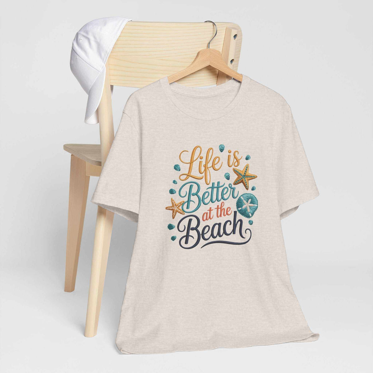 Life is better at the beach shirt in light beige with colorful coastal lettering, seashells, and starfish graphic