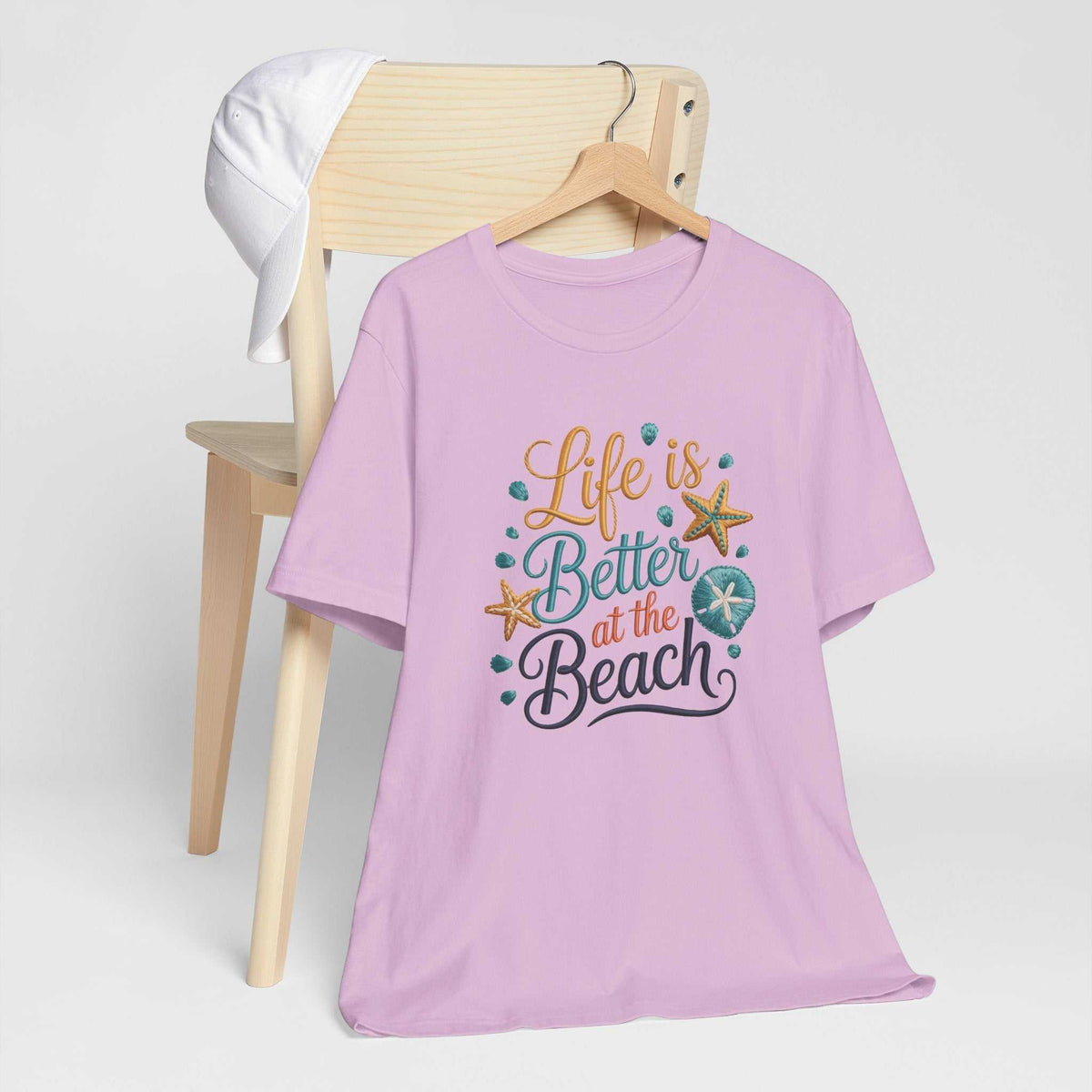 T-shirt featuring life is better at the beach in colorful lettering with seashells and starfish on a lavender crewneck.