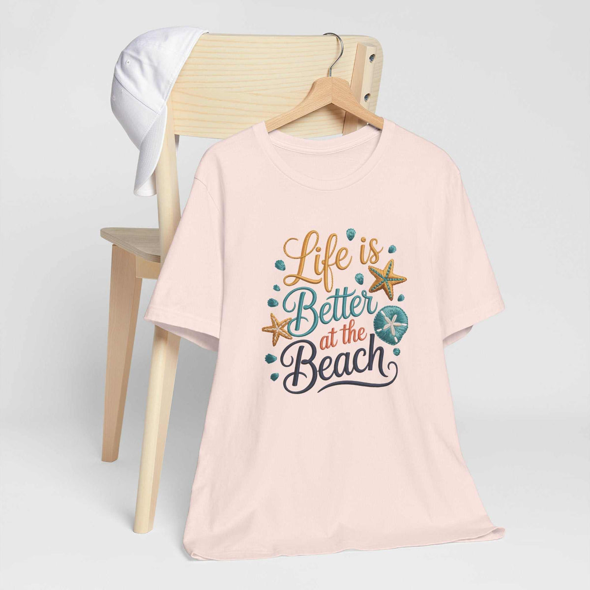 T-shirt in pale pink with a colorful “life is better at the beach” graphic, seashells and starfish