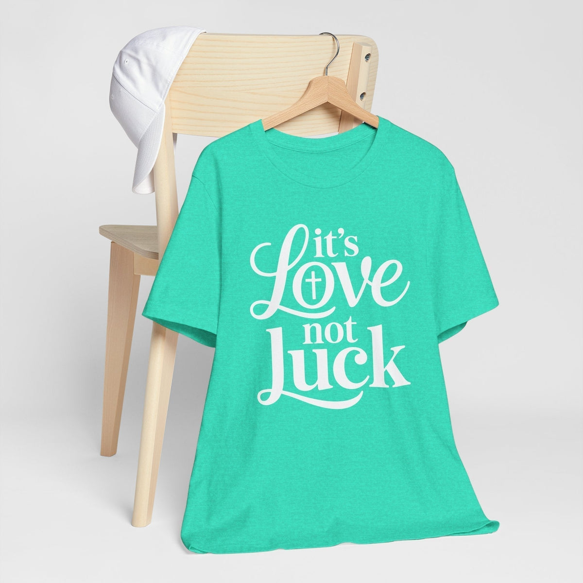 Graphic tee in turquoise cotton with white script and serif lettering reading “It’s Love Not Luck,” a love in faith shirt.