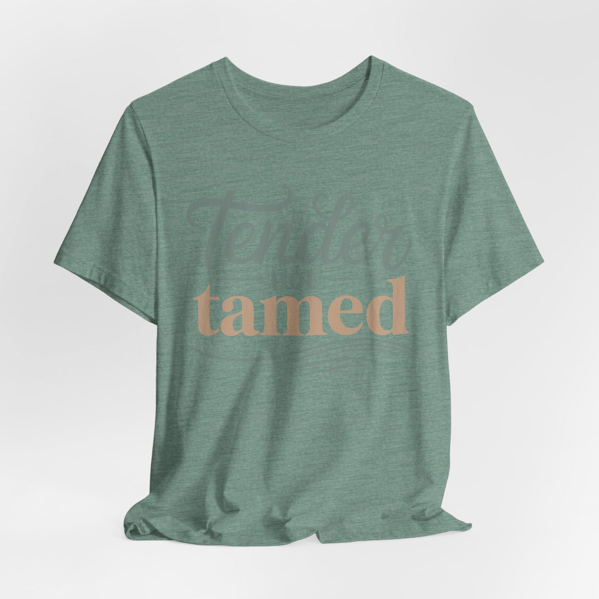 motivational graphic tee in heather sage green with soft script reading “Tender Not Tamed” across the front