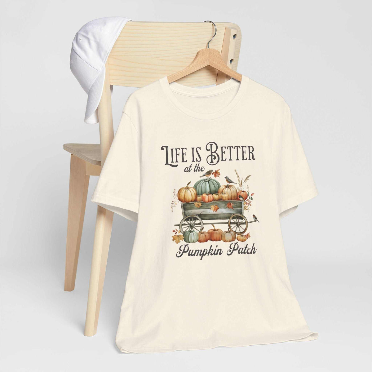 Pumpkin patch tshirt in cream cotton with vintage lettering, a pumpkin-filled wagon, autumn leaves, and a small bird.