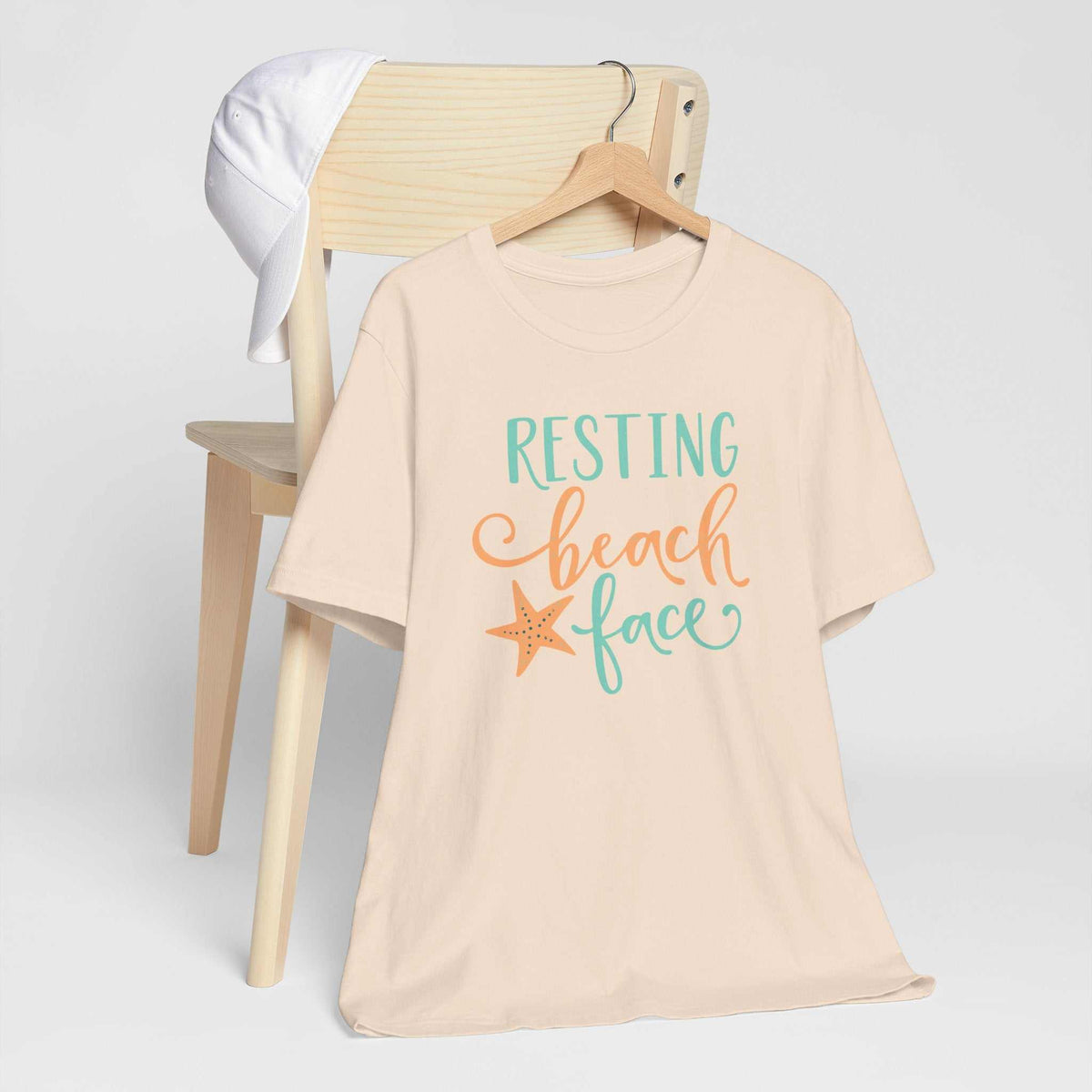Resting Beach Face graphic T-shirt in pale peach cotton with turquoise and coral lettering and a starfish design