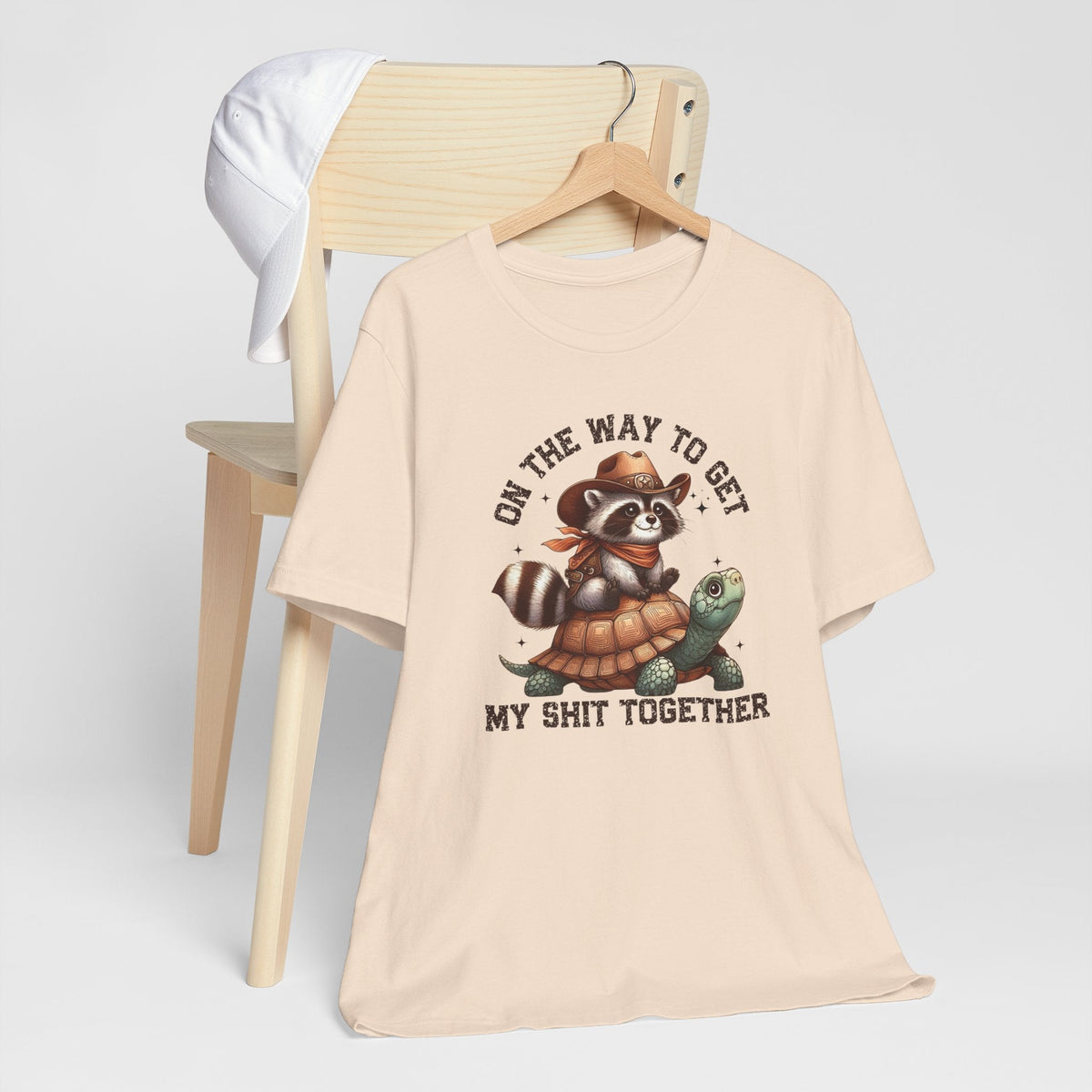 Sassy tee shirt in soft cream cotton with a vintage-style cowboy raccoon riding a turtle graphic and humorous lettering