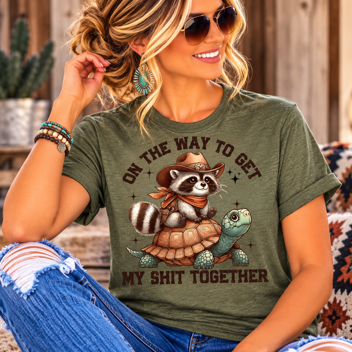 sassy tee shirt in olive green with a cowboy raccoon riding a turtle and humorous western lettering