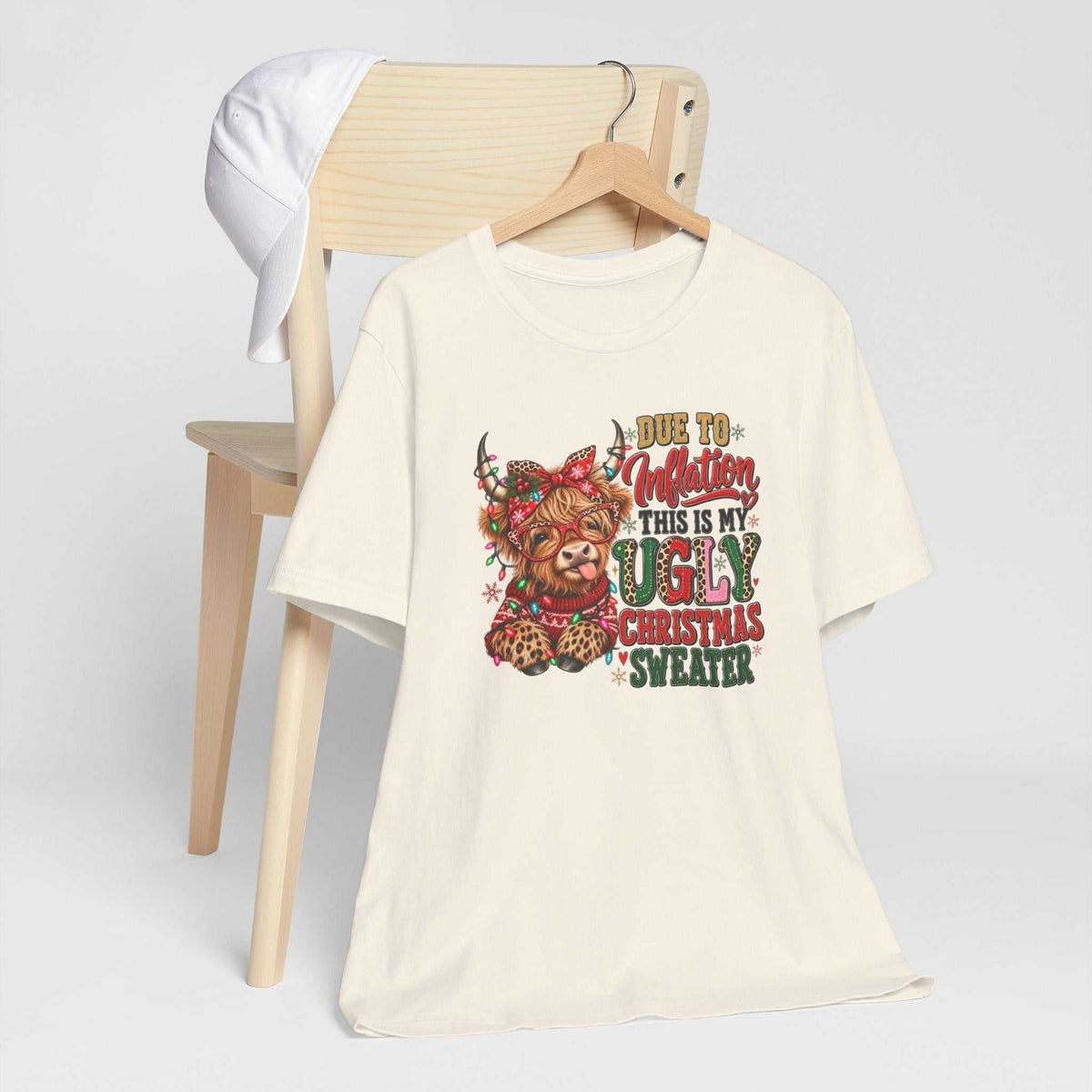 ugly christmas shirt in ivory cotton with a colorful Highland cow, leopard print, festive lights and holiday lettering